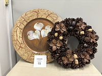 Wooden painted plate leaning against wall with pine cone wreath placed in front