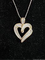 Close-up of heart-shaped pendant on black background showing gold finish and diamond settings.