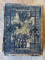 Front cover of the antique Holy Bible showing heavy wear and gold embossed title with ornate embossed decoration on cover.