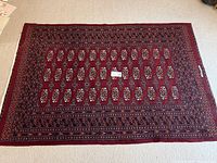 Photo showing one of the rectangular red Bokhara rugs with geometric medallion patterns laid flat on carpet.