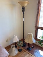 Antique floor lamp with amber glass torchiere shade standing next to three smaller table lamps with varied bases and shades.