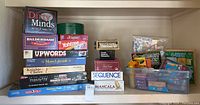 Full view of all board games and kits stacked on a shelf including boxes and plastic containers.