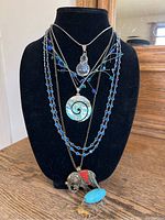 Photo shows multi-strand layered necklace with blue beads, silver chains, and a large fish-shaped turquoise pendant with red accents.