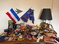 Photo of table top displaying a black CU football helmet lamp with lampshade, various flags, card trick set, toys, and small collectibles.