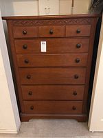 Full front view of tall wooden dresser showing five drawers and carved decorative trim beneath top surface