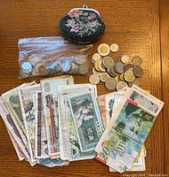 Overview of various foreign banknotes fanned out with some coins and a coin purse on a wooden surface.