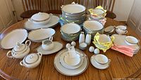 Full set displayed on wooden table with chairs in room background. Various plates stacked and small items placed in front.