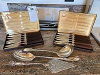 Photo of two knife sets in original boxes along with three silver-toned serving utensils on countertop