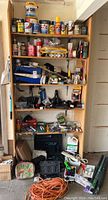 Full view of shelves organized with paint cans, cleaning supplies, tools, boxes and accessories in a garage environment.