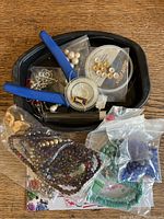 Overview of the assorted beads and jewelry making tools in a black container and several plastic bags.