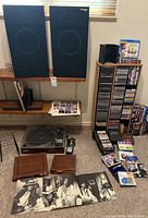 Wide view showing speakers atop wooden shelves, record player below, stacks of CDs and vinyl albums on floor