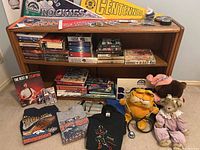 Front view of solid wood bookcase filled with books, DVDs, plush toys, and folded t-shirts arranged on and in front.