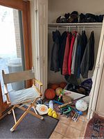 Wide view of sports equipment, coats on hangers, basketballs, baseball bats and gloves, soccer ball, and other sports accessories on the floor under the coats in a small closet area