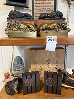 Shelf with brass and iron lion bookends and other collectibles including black panel bookends, carved figures, and a painted wooden horse.