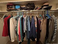 Wide view of clothes hanging on a rod and hats on shelf above