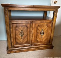 Front view of wooden buffet table showing paneled cabinet doors with ring pull handles and carved corner details.