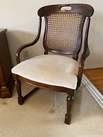 Front and side view of wooden chair with beige upholstered seat, cane backrest, and curved arms.