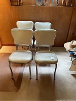 Four matching white vinyl chairs with metal legs, arranged in two rows of two, shown from front angle.