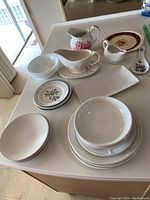 Overall lot on kitchen counter including various plates, bowls, two gravy boats, and a spoon rest spaced for display.