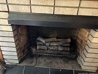 Electric fire insert installed in a brick fireplace showing artificial logs inside the firebox and power cord on the floor.