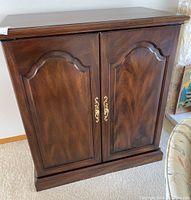 Front view of wooden entertainment unit with ornate cupboard doors and brass handles