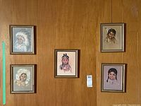 Five framed prints hanging on a wooden paneled wall arranged in a group of four with one centered below