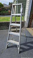 Front view of the 5 foot aluminum ladder showing 4 steps and top platform, placed outdoors on pavement.