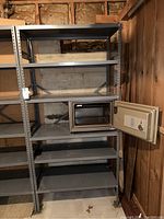 View of full gray metal storage shelf showing all five shelves and small safe on one shelf