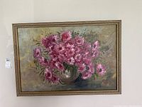 Framed oil painting featuring a bouquet of pink flowers in a vase with signature visible in lower right corner, against muted background.