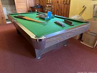 Side angle view of the pool table showing green felt surface and wood finish sides with metal corner protectors