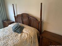 Front view of wood bed frame with rattan inset headboard and two matching nightstands, bed made up with beige quilt and pillows.