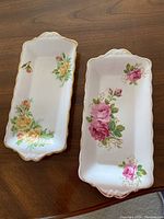 Two rectangular Royal Albert bone china trays on a wooden table, one with yellow rose pattern and one with pink rose pattern.