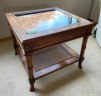 Side view of the wooden side table showing the glass top, carved legs, and cane shelf.