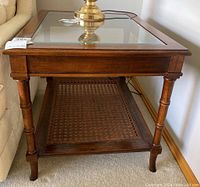 Side view of wooden side table showing glass top and cane woven shelf, placed next to sofa.