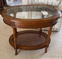 Front view showing oval wood and glass top with cane shelf below and turned legs