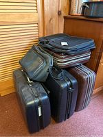 Stack of four suitcases and two bags in a corner near wooden furniture