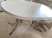 Top view of round dining table with inserted leaf, showing white table surface and seam line where the leaf is inserted.