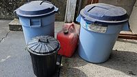 Three trash bins and one red jerry can arranged outside a garage space, showing dirt and dust on surfaces.
