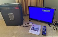 Photo showing RCA 19-inch TV monitor powered on with 'No Signal' screen, black paper shredder to left, instruction manual and remote placed in front of TV.