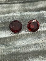 Top-down view showing two round garnet gemstones with deep red coloration laying on a soft textured surface.