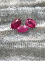 Three oval faceted rubies on textured fabric, showing color and cut variations
