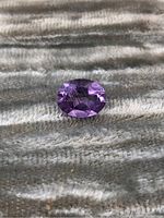 Photo of an oval faceted amethyst gemstone showing front view and color hue.