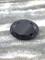 Oval cut black sapphire gemstone with faceted surface showing reflection and color in natural light.