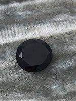 Close-up view of oval faceted black sapphire gemstone showing surface and facets.
