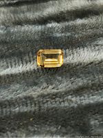 Top view of rectangular emerald cut citrine gemstone on a textured dark gray fabric background showing color and facets.
