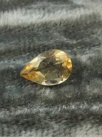 Front view of pear-shaped citrine gemstone showing facets and clarity on textured gray fabric background.