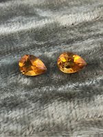 Two pear-shaped faceted citrine gemstones on textured surface showing front view with internal reflections and color.