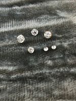 Front view of six loose diamonds on a dark, textured background showing size and condition.