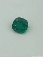 Front view of emerald gemstone showing its cushion cut faceting and vibrant green color.