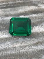 Photo of emerald cut green gemstone on textured background showing front view and facets.